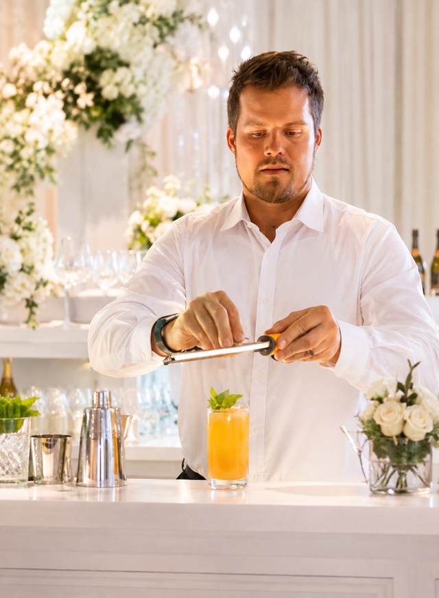 Christopher Rice, founder of Make It a Double, grating a garnish over a cocktail at a white event bar