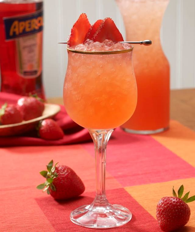 Gold-rimmed stemmed glass of strawberry aperitivo with a strawberry skewer garnish