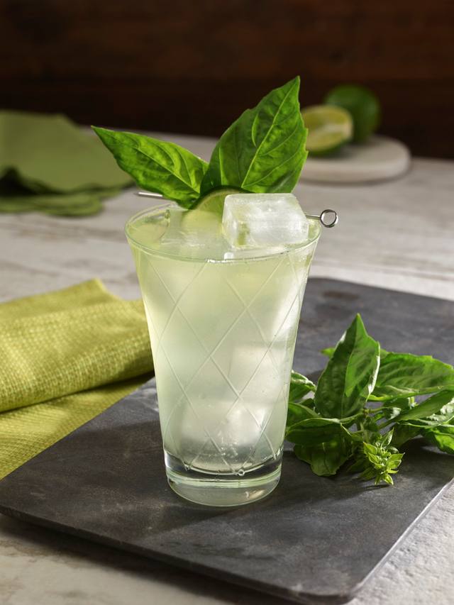 Cut glass tumbler of a basil smash with a clear ice cube and fresh basil leaves