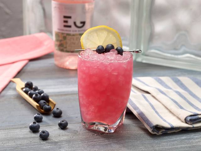 Short glass of pink blueberry lemon crush over pebble ice with a lemon wheel and blueberry pick