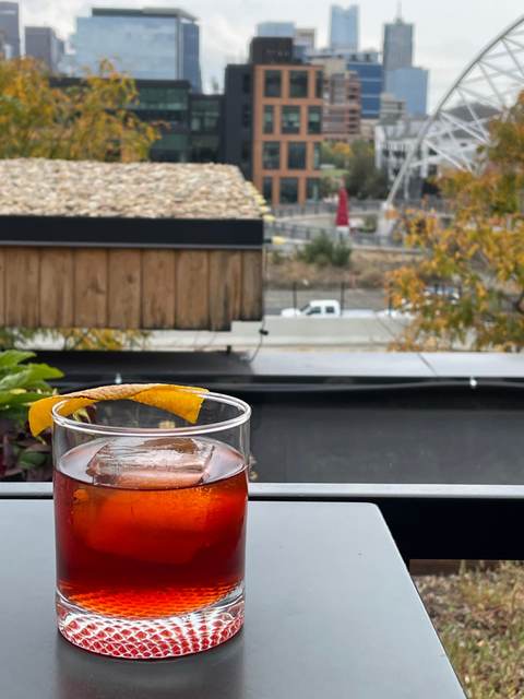 Chocolate Boulevardier over a large clear cube with an orange twist on a rooftop table