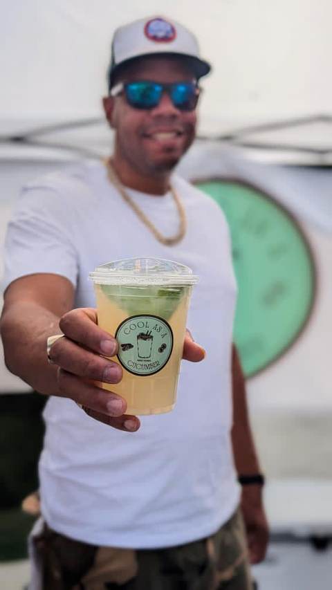 Guest holding out a Cool as a Cucumber mocktail in a branded cup at an outdoor event