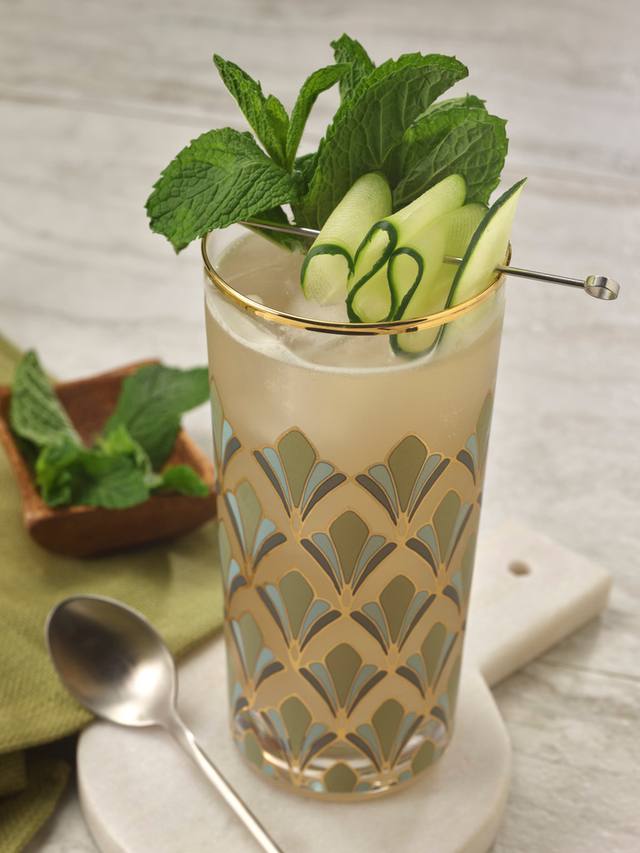 Deco patterned highball of a cucumber mint collins with a cucumber ribbon and mint bouquet