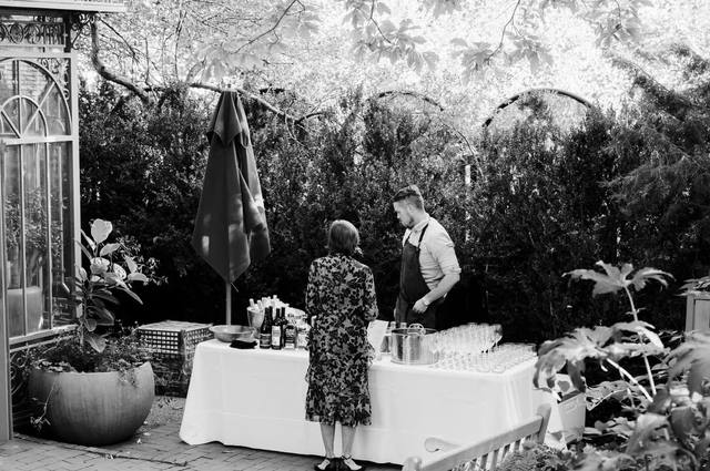 Black and white photo of a bartender serving a guest at an outdoor garden bar setup