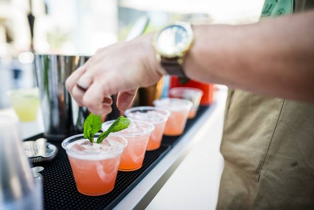Bartender placing fresh mint into a line of pink cocktails on a bar mat