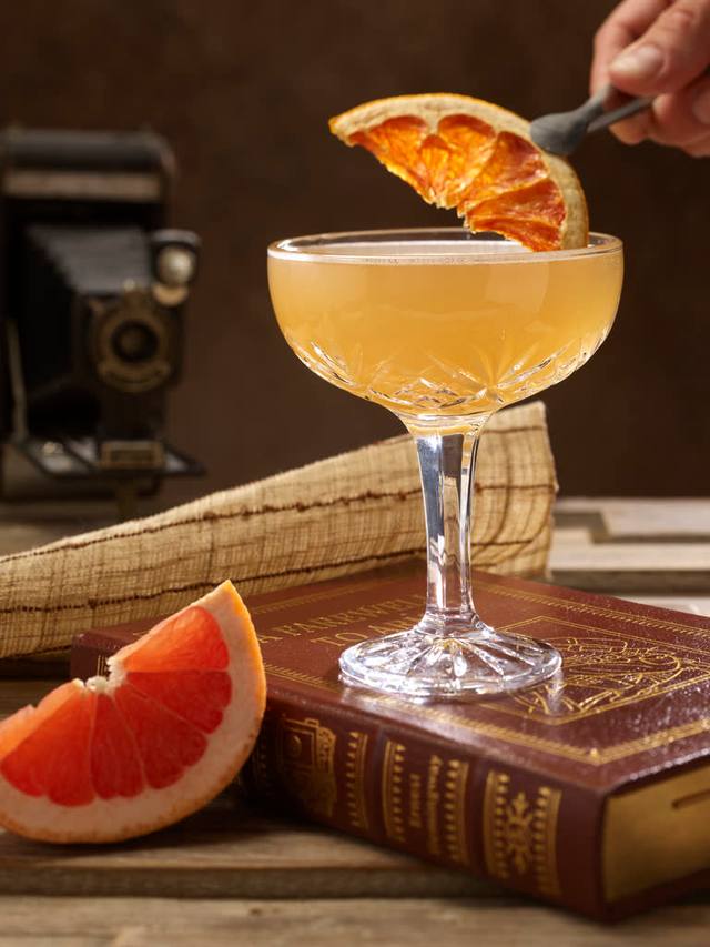 Vintage coupe of a citrus cocktail being garnished with a dehydrated grapefruit wheel
