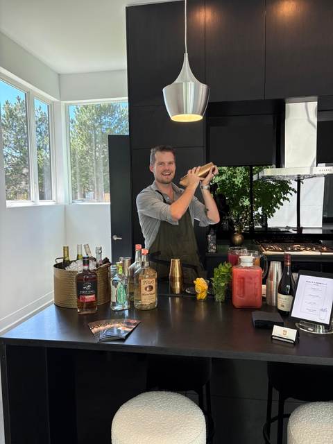 Bartender shaking a cocktail behind a home kitchen island bar set with glassware