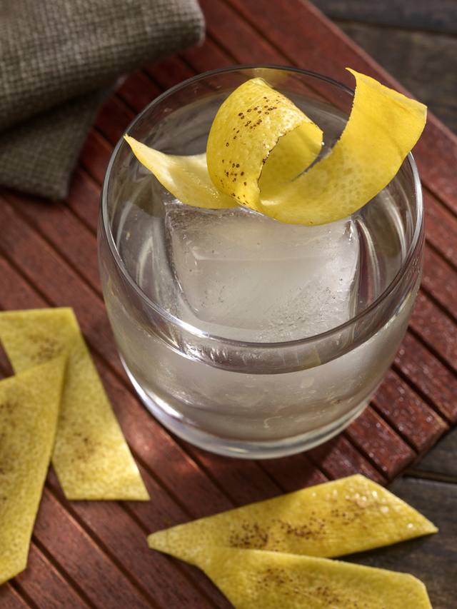 Rocks glass with a clear spirit, single large ice cube and a wide lemon twist