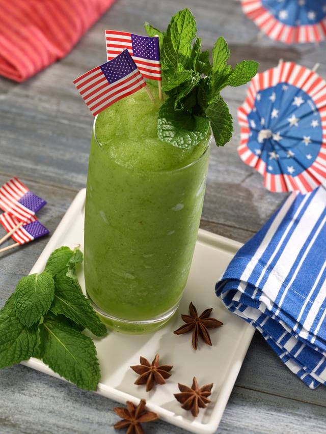 Frozen green mint frappe in a tall glass with mint sprigs and small American flags