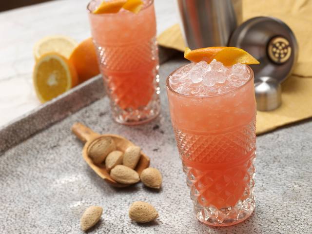 Two cut crystal highballs of an orange almond cooler with orange peel garnish