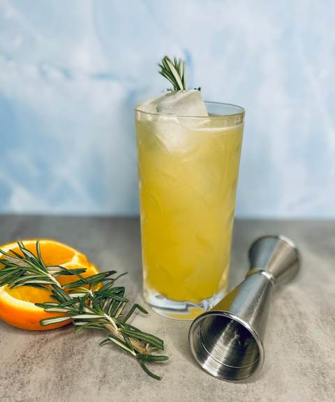 Peach and rosemary highball over a clear ice spear with an orange wheel and jigger