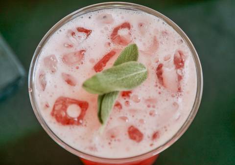 Overhead close up of a pink sage crush mocktail with crushed ice and a fresh sage leaf