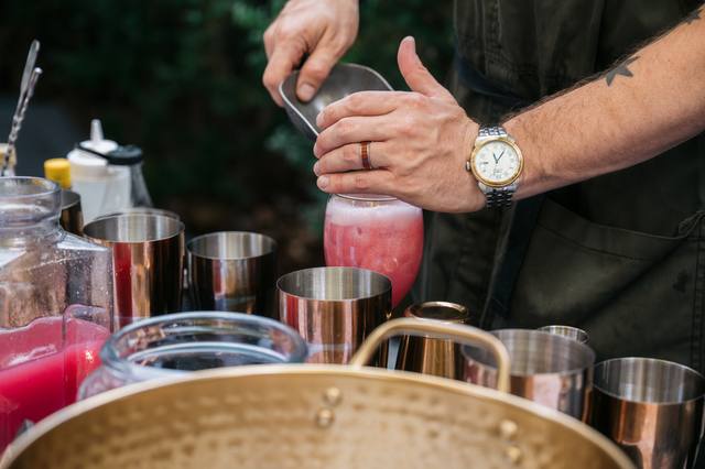 Bartender straining a pink cocktail from a shaker into copper cups at an outdoor bar