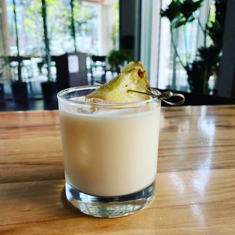 Smoked Pina Colada in a rocks glass with a charred pineapple wedge on a wooden bar top