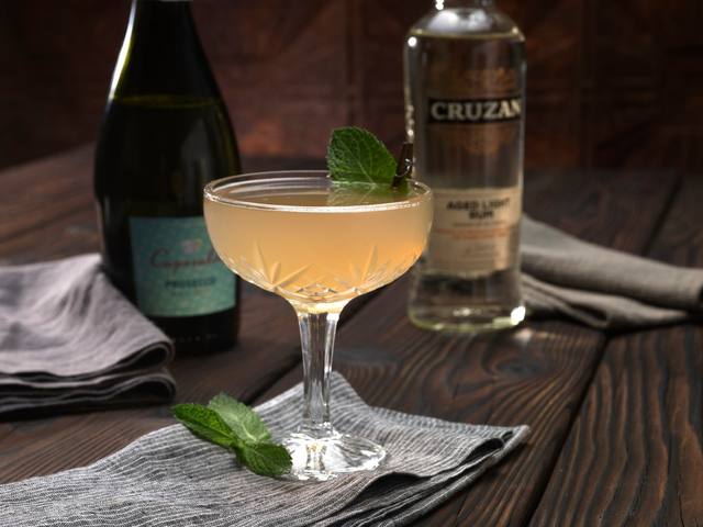 Crystal coupe of a sparkling rum cocktail garnished with a mint leaf