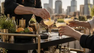 Bartender garnishing coupe cocktails on a brass mobile bar at an outdoor Denver pop-up as guests reach for drinks
